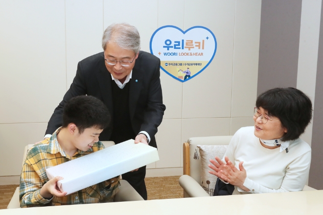 우리금융그룹 우리금융미래재단은 지난 2일 서울 중구에 있는 우리금융 본사에서 ‘우리 루키(Look & Hear) 프로젝트’를 통해 시·청각 수술비를 지원받은 수혜자와 가족 12명을 초청해 새해맞이 행사를 가졌다고 3일 밝혔다. 사진은 임종룡 우리금융그룹 임종룡 회장(가운데)이 초청 가족에게 선물을 전달하고 있는 모습. (사진 = 우리금융미래재단 제공)