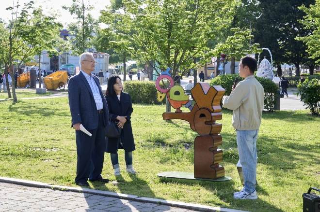 지난 16일 서울 한강뚝섬공원에서 열린 견생조각전 100회 기념전에서 윤영달 크라운해태제과 회장(왼쪽)과 김정희 한국조각가협회 이사장이 이용태 작가의 Talking parrot 작품 설명을 듣고 있다. / 사진=크라운해태 제공