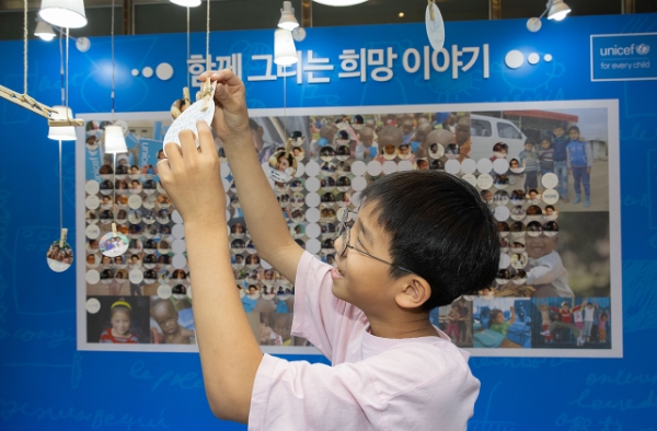 유니세프 한국위원회 ‘함께 그리는 희망 이야기’ 특별전의 희망 트리에 서울 흥인초 4학년 장주원 학생이 희망 메시지를 걸고 있다. (사진제공=유니세프 한국위원회)