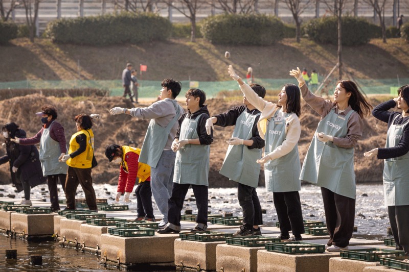 코웨이 임직원 봉사자가 안양천 다리에서 EM 흙공을 던지고 있다.