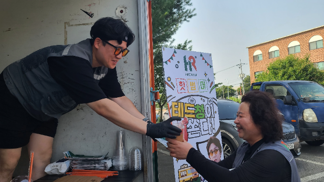 HR그룹의 이재승(청) 님이 지난 8일 청주1 모바일 캠프에서 퀵플렉서 기사에게 시원한 수박주스를 건네며 함께 웃음 짓고 있다./사진=HR그룹(주)미디어팀 제공