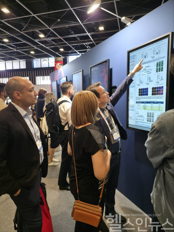 호필수 샤페론 전무가 2025 유럽 피부과학회의 샤페론 포스터 앞에서 참석한 연구자들에게 원형탈모치료제 연구결과를 설명 중 (사진 제공=샤페론)