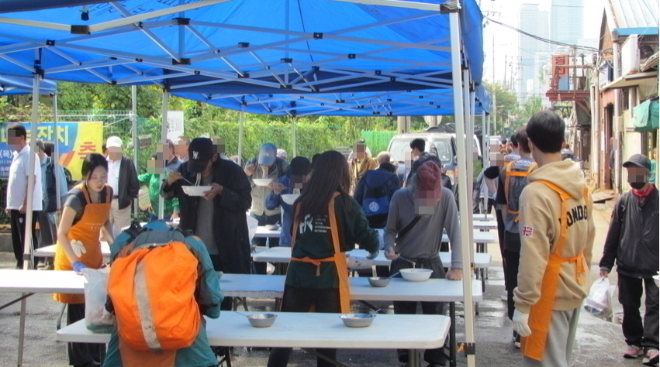 추석을 앞두고 서울 영등포 쪽방촌에서 HR그룹 임직원과 봉사자들이 천막 아래 마련한 배식대에서 잔치국수를 대접하며 어르신들과 이웃들이 함께 식사하고 있다./사진=HR그룹(주) 미디어팀 제공