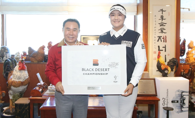 제너시스BBQ 그룹이 후원하는 LPGA 투어 프로골퍼 유해란 선수가 2026 시즌 출정을 앞두고 본사를 방문해 윤홍근 회장을 비롯한 임직원들을 만나 지난해의 성과에 대한 감사와 새 시즌 목표를 공유하는 시간을 가졌다. 사진은 유해란 선수가 지난해 우승한 블랙데저트 대회 당시 우승 홀 깃발에 사인과 다짐을 적어 윤홍근 회장에게 전달하는 모습