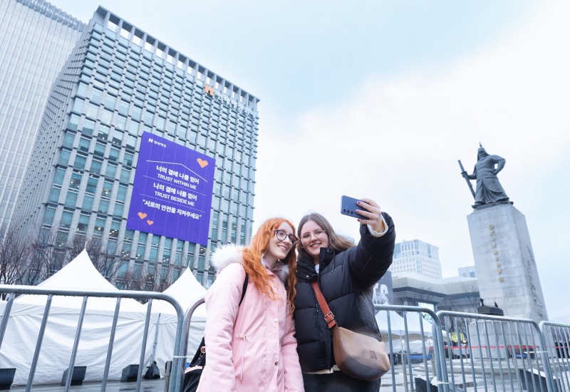 18일 서울시 종로구 현대해상 본사 외벽의 방탄소년단 노래 가사를 인용한 ‘신뢰와 안전’ 메시지를 배경으로 외국인 방문객들이 사진을 촬영하고 있다.