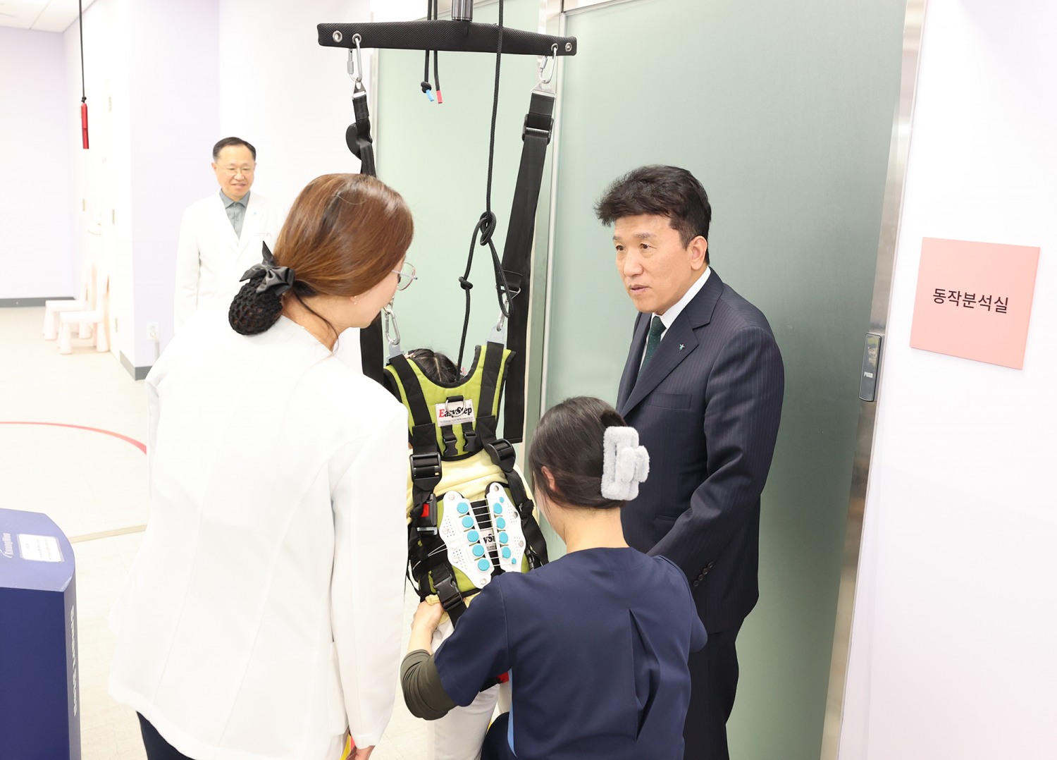 이날 전달식에 참석한 함영주 회장(사진 맨 오른쪽)이 워킹레일 보행치료를 받고 있는 장애 아동에게 따뜻한 격려의 말을 전하고 있다.